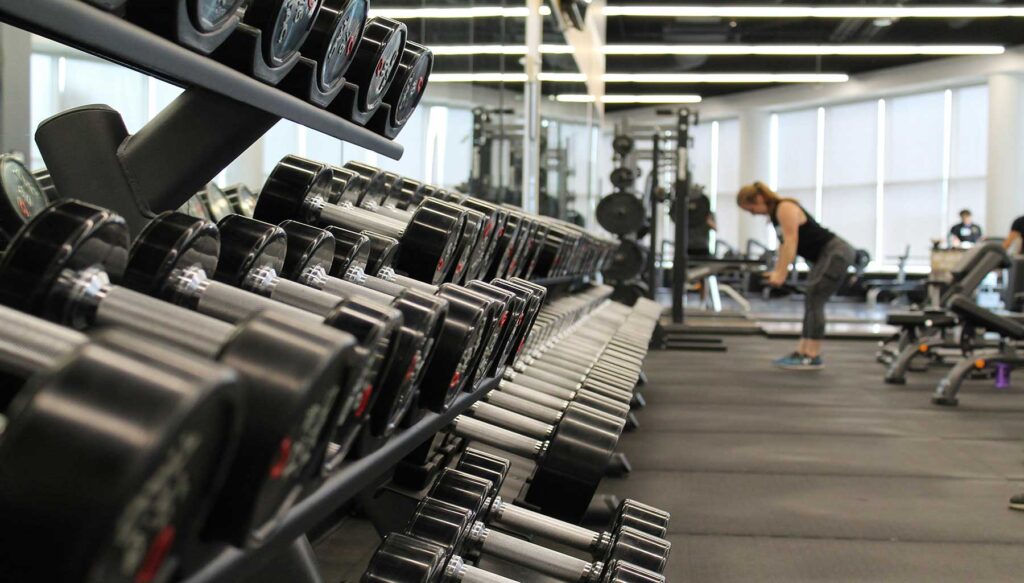 People of diverse backgrounds exercising at a gym, using various equipment like treadmills and weights.